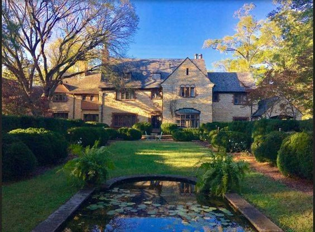 Stone mansion rear view with manicured gardens, boxwood hedges, and reflective lily pond