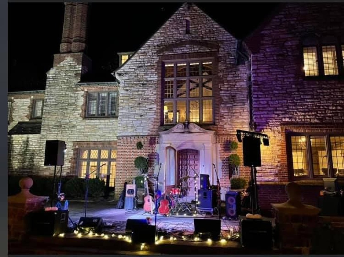 Live band stage set up at night in front of stone mansion with purple and warm uplighting
