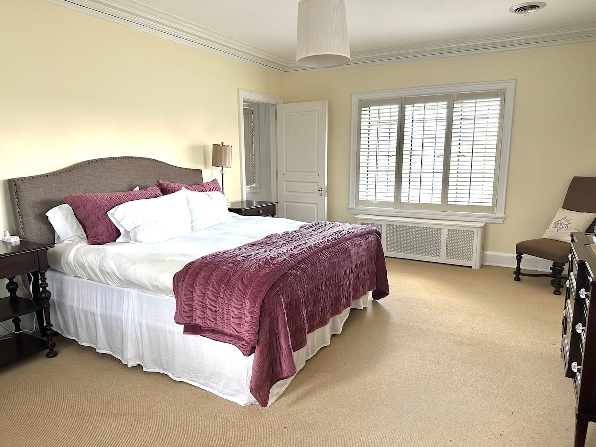 King bedroom with purple throw and plantation shutters