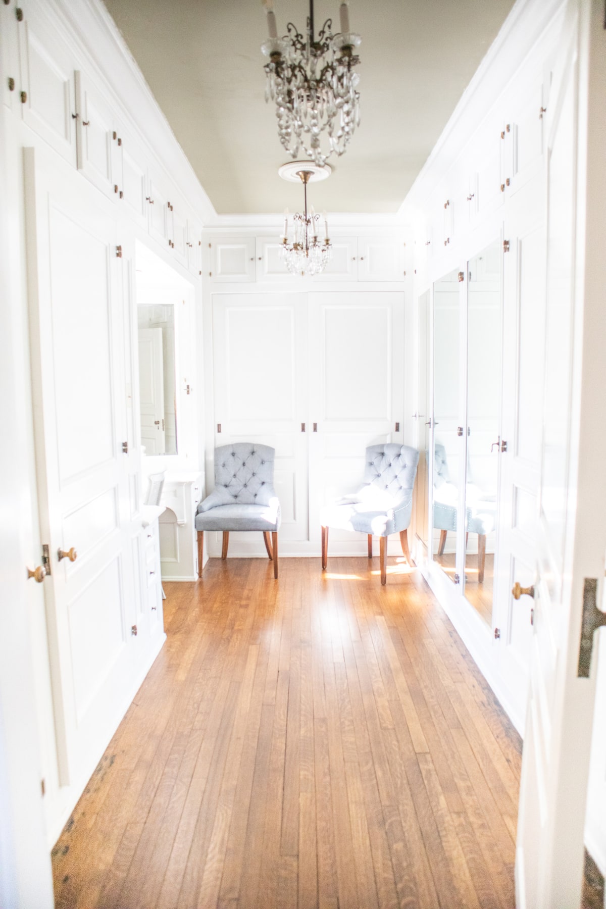 Luxury walk-in closet with white cabinetry and chandeliers