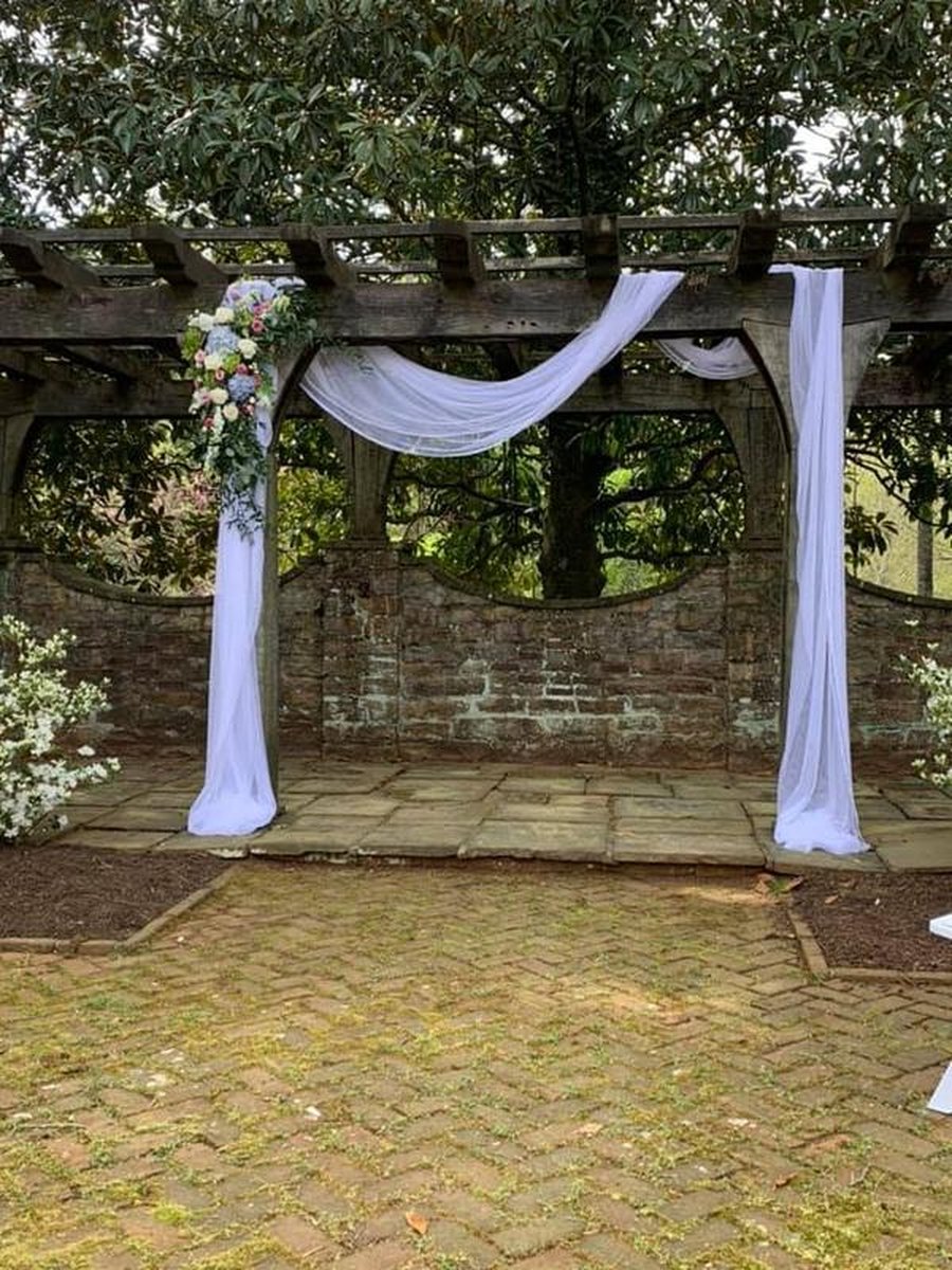 Rustic wooden pergola draped with white fabric and floral arrangement on brick patio
