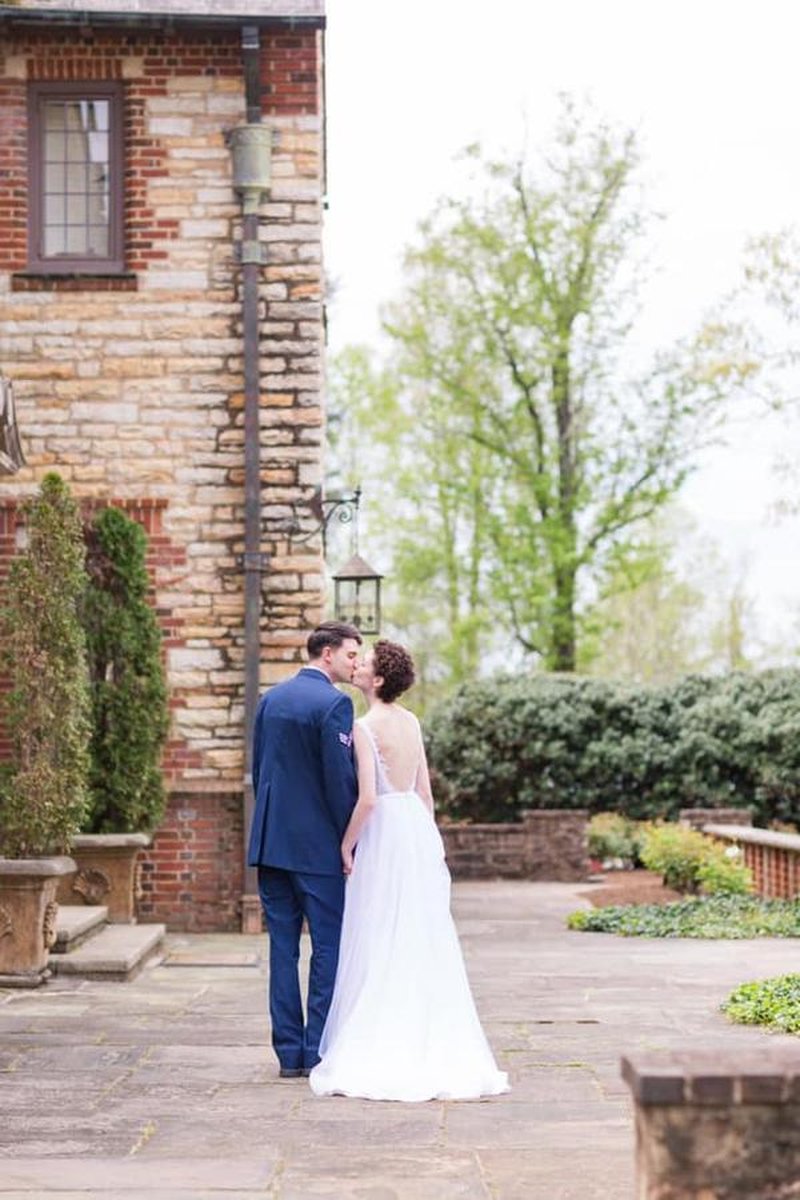 Bride and groom kissing on stone patio beside brick and stone mansion exterior
