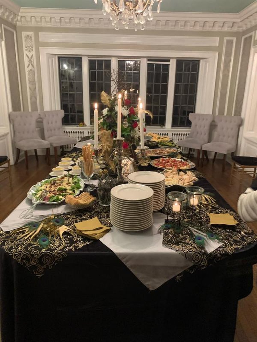 Elegant buffet spread in mansion dining room with candles, peacock feathers, black-and-gold linens
