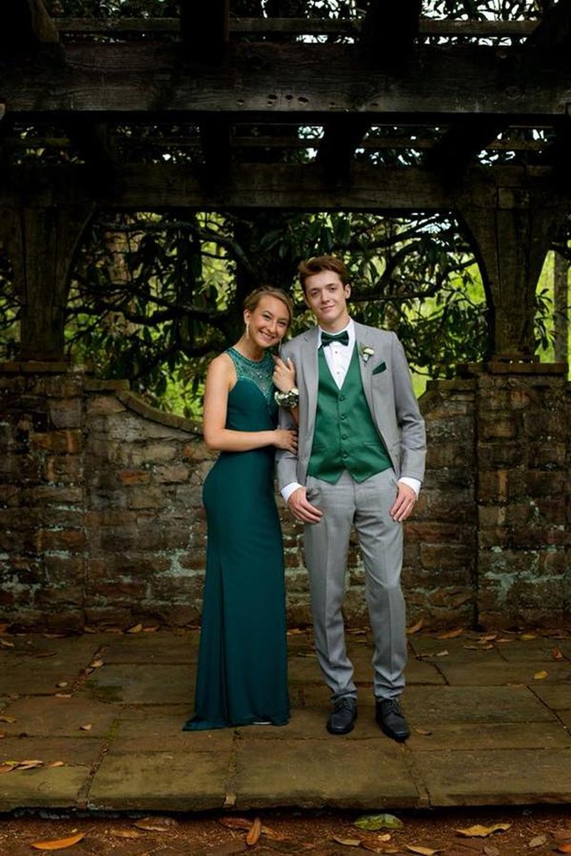 Couple in formal attire posing under rustic stone and wooden pergola