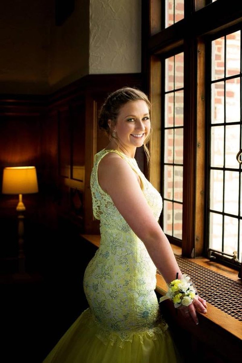 Young woman in yellow beaded gown with wrist corsage posing by window in mansion