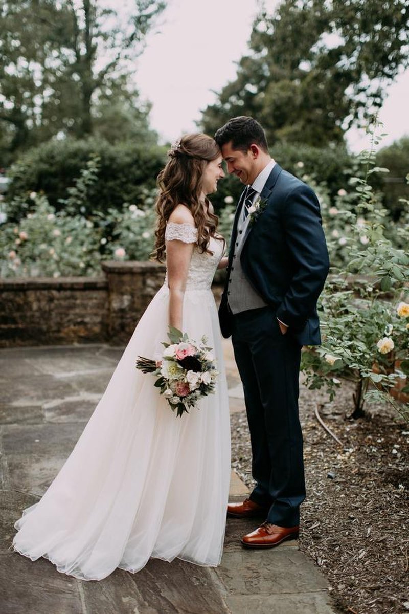Bride and groom touching foreheads in rose garden on stone pathway