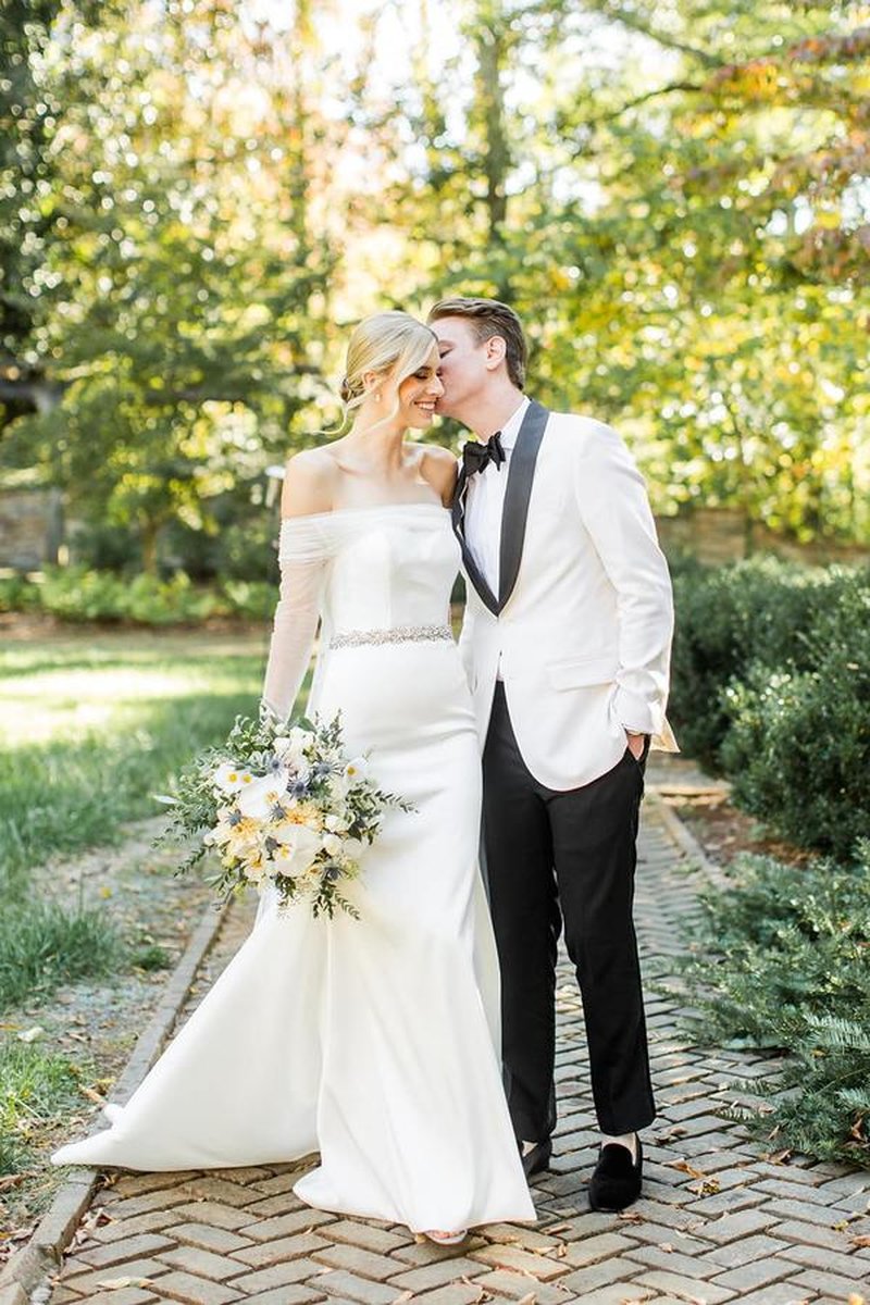 Bride and groom walking on brick path in garden, bride holding bouquet