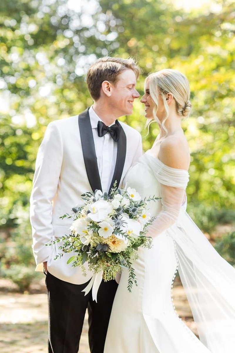 Close-up of bride and groom smiling at each other outdoors with lush green bokeh