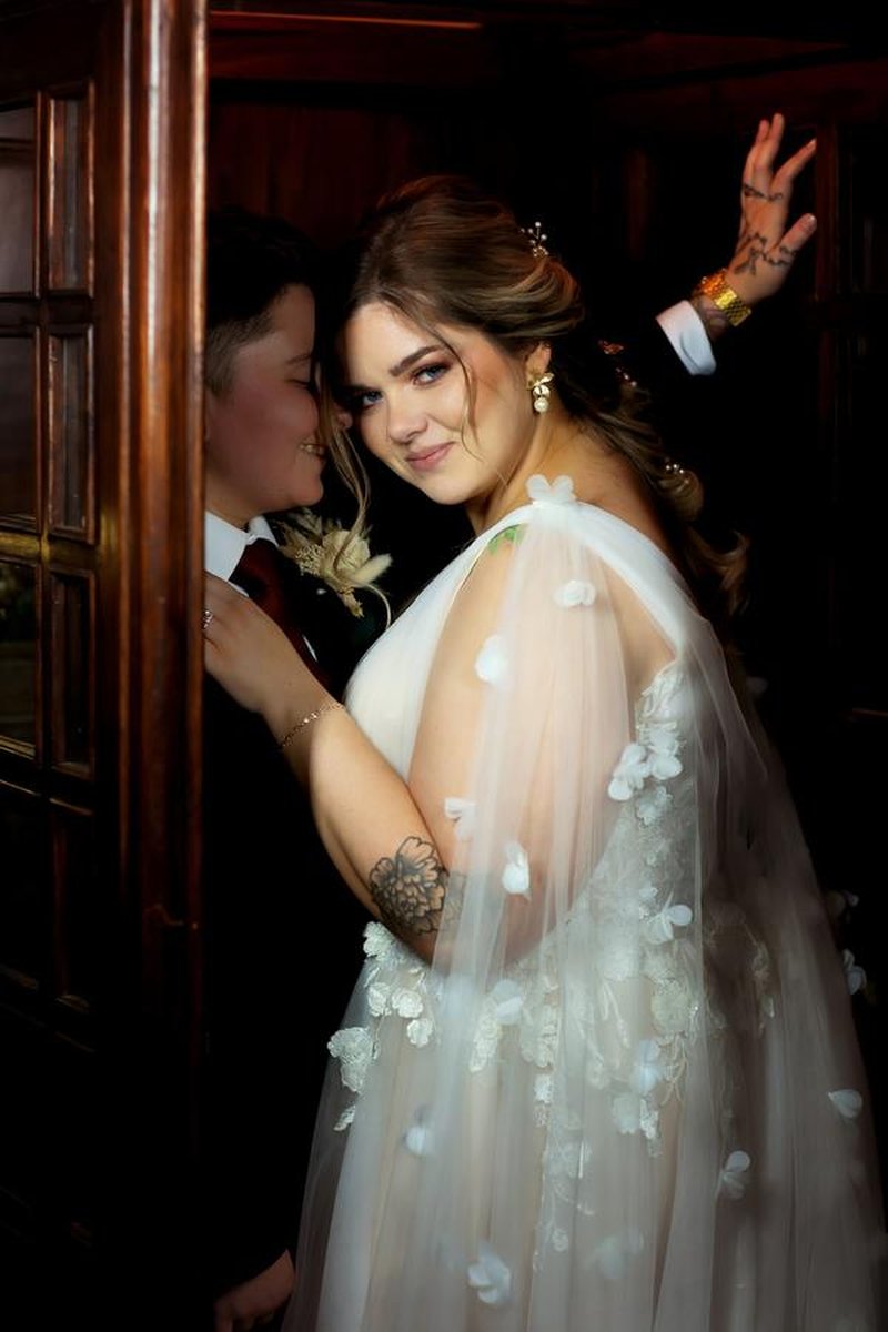Couple embracing in doorway, bride in floral tulle gown against dark wood paneling