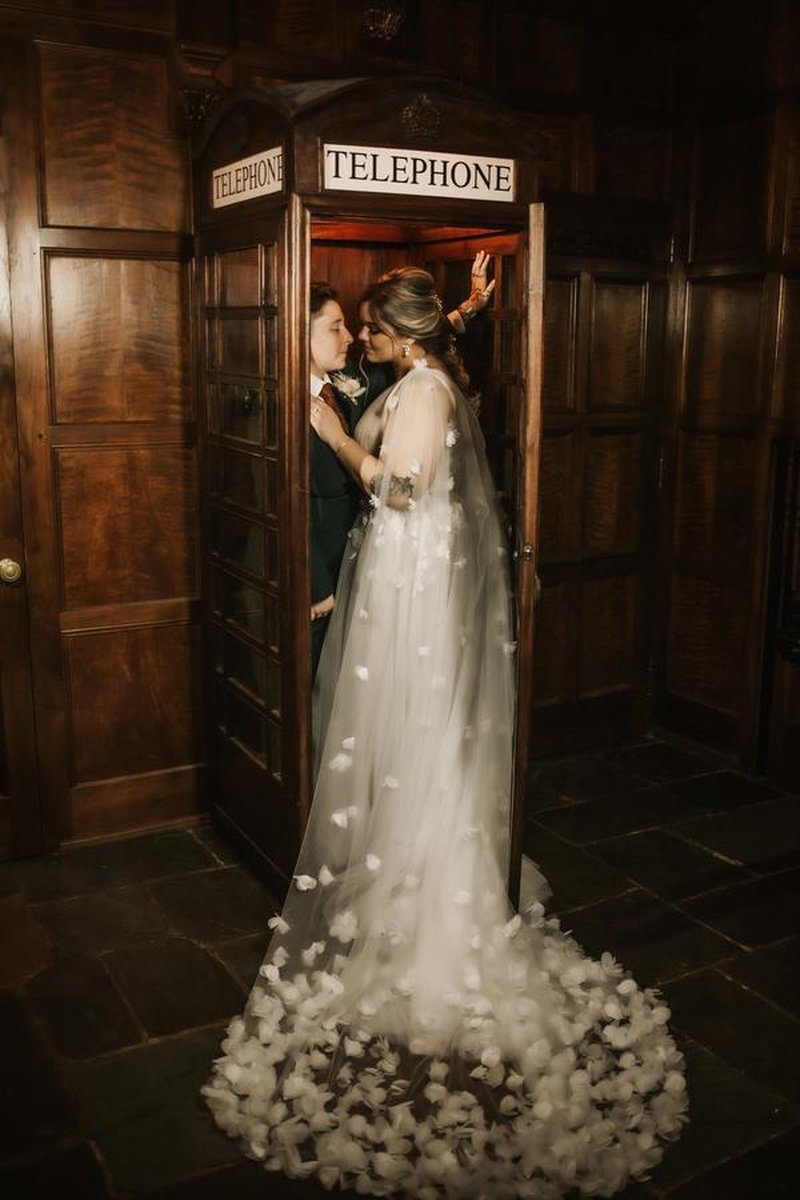 Couple posing inside vintage wooden telephone booth in wood-paneled mansion room