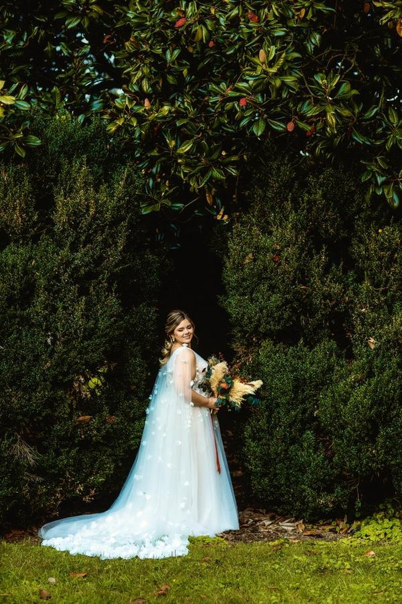 Bride posing with bouquet in front of lush boxwood hedge and magnolia tree