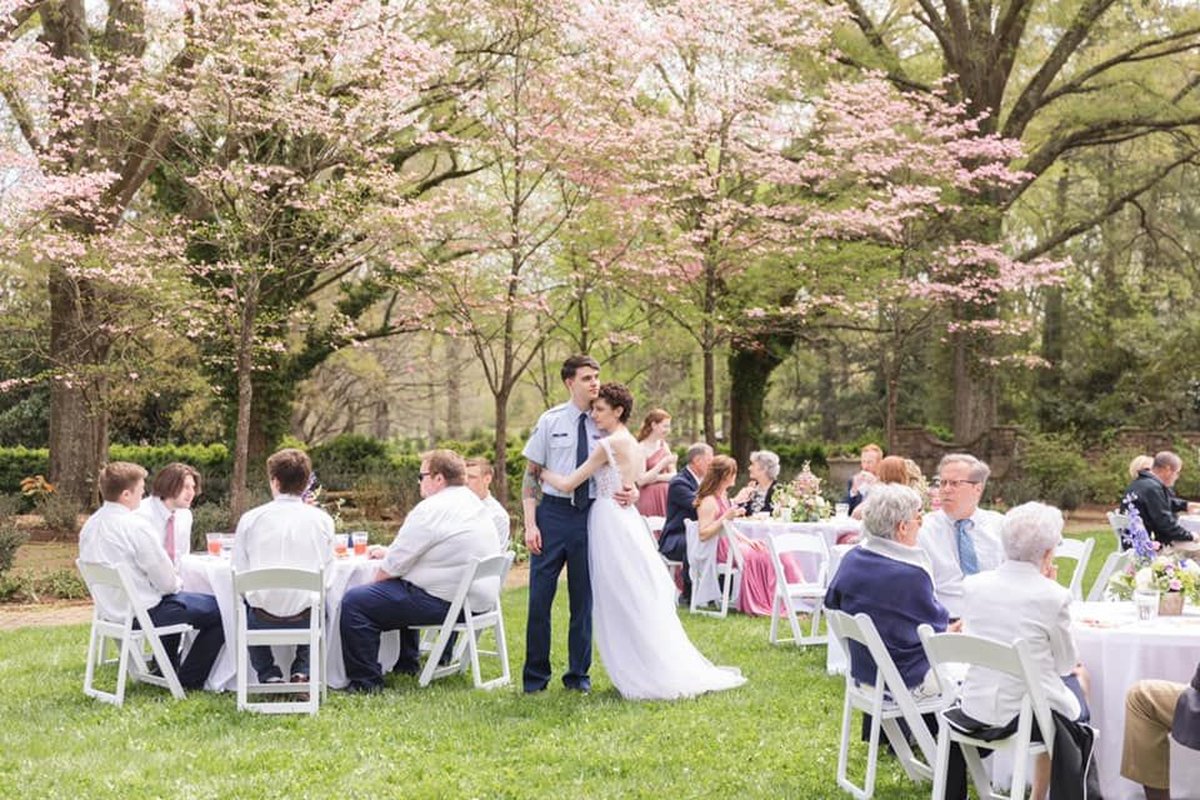 Couple's first dance at outdoor garden reception under pink dogwood trees with seated guests